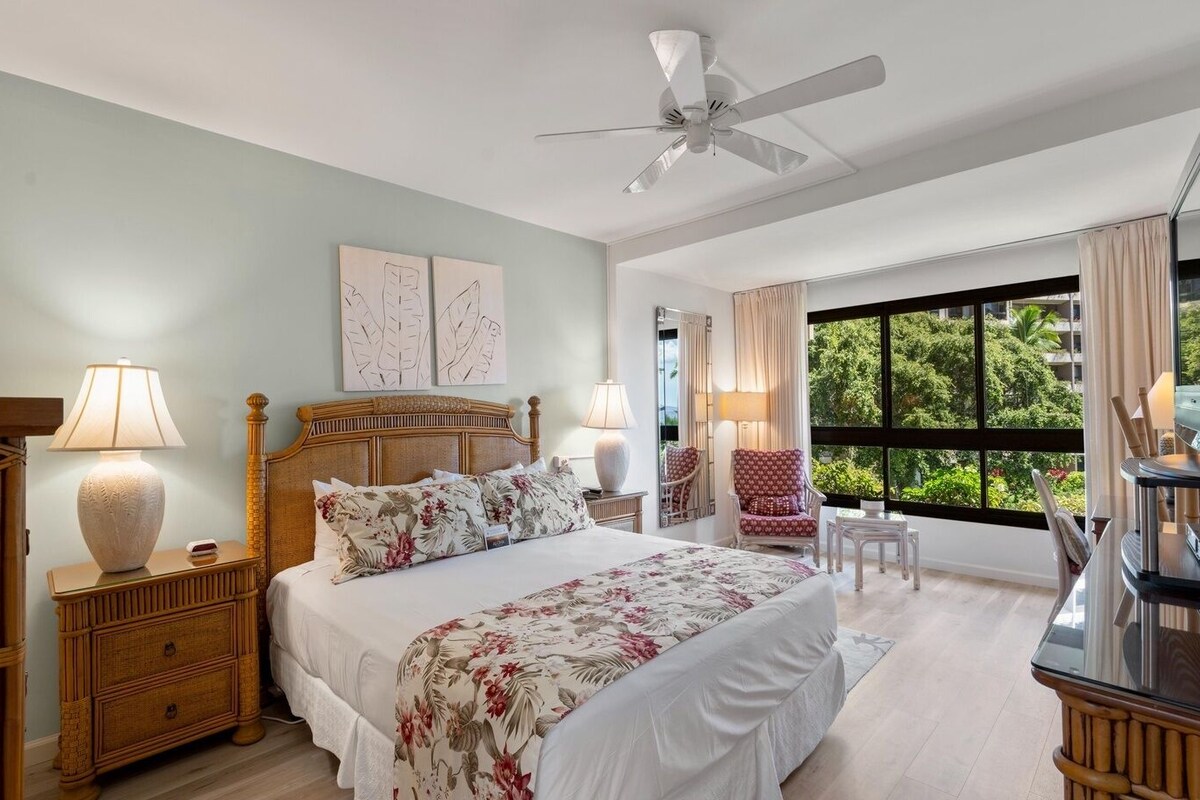 A hotel room with a bed, two bedside tables, a chair, a desk, a ceiling fan, and a large window with a view.