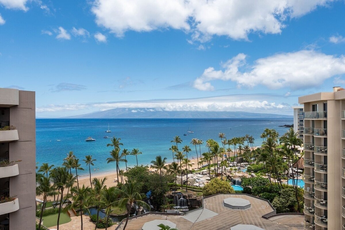 A resort with a pool, palm trees, and a view of the ocean.