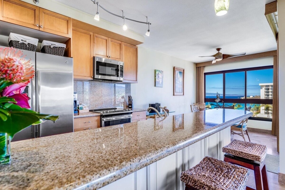 A modern kitchen with granite countertops, stainless steel appliances, and a view of the ocean.