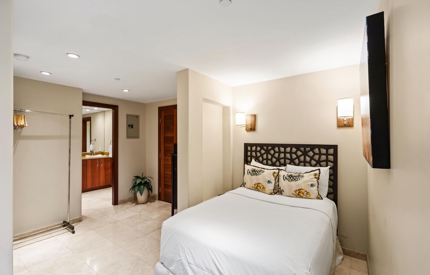 A hotel room with a bed, a bathroom, a hallway, and a potted plant.