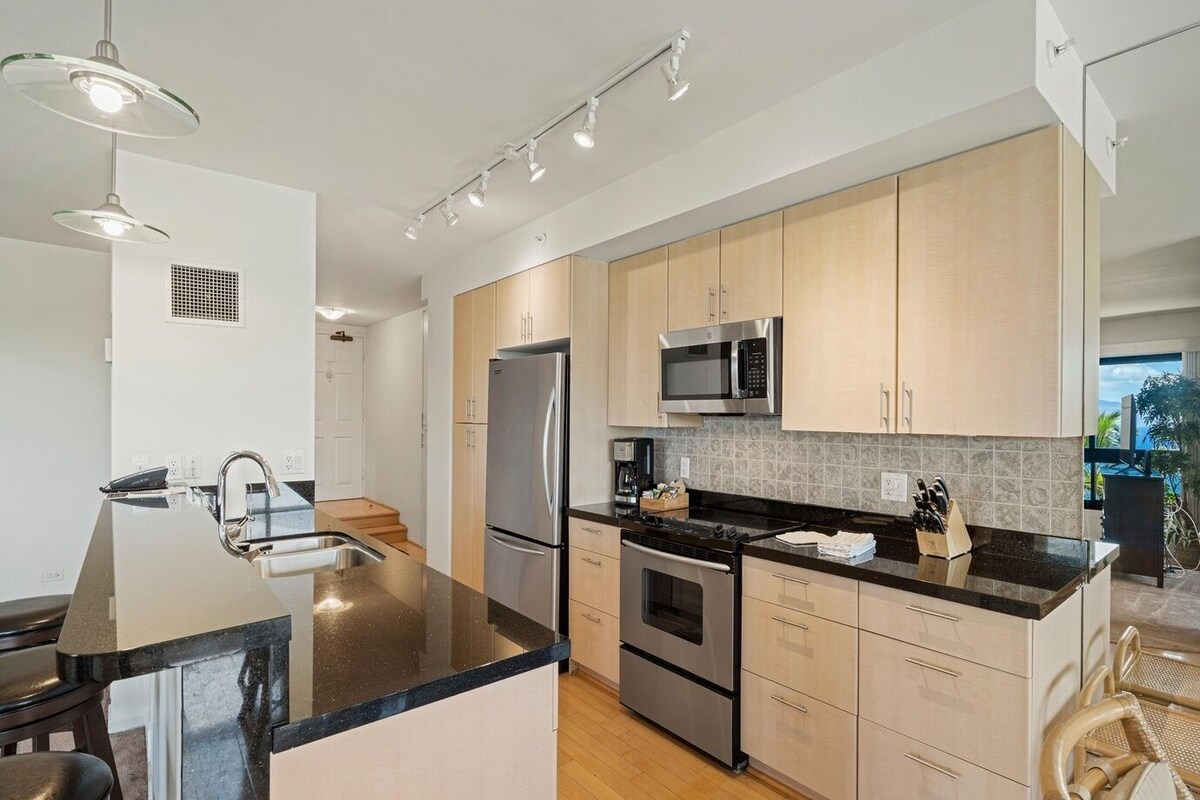 A modern kitchen with stainless steel appliances, a black countertop, and wooden cabinets.