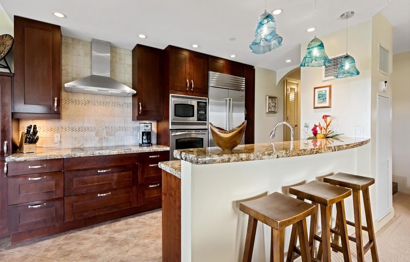 A modern kitchen with dark wooden cabinets, stainless steel appliances, a marble countertop, and a central island with stools.