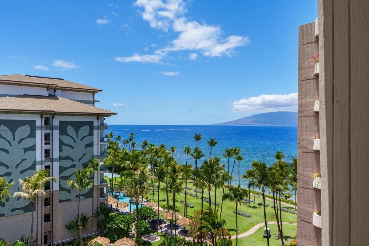A resort with a pool area, palm trees, and a view of the ocean.
