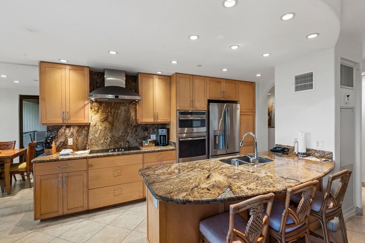 A modern kitchen with granite countertops, stainless steel appliances, wooden cabinets, and a central island with seating.