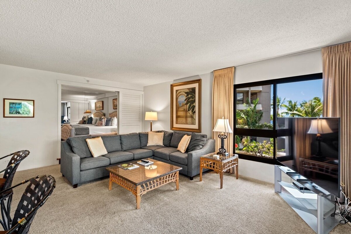 A hotel room with a sofa, coffee table, TV, and a view of palm trees.