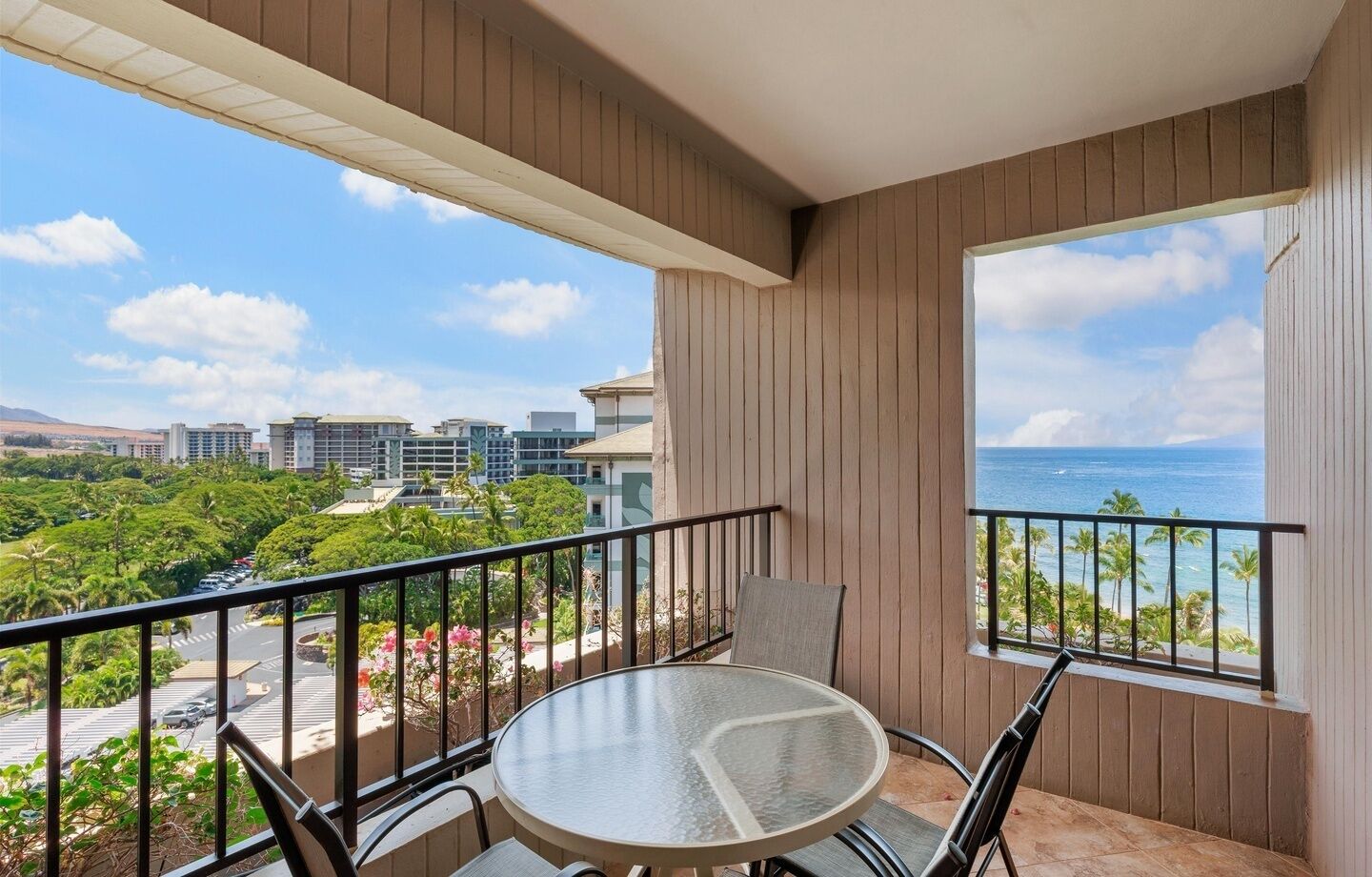 A balcony with a round table and chairs, a view of the ocean, and buildings in the background.