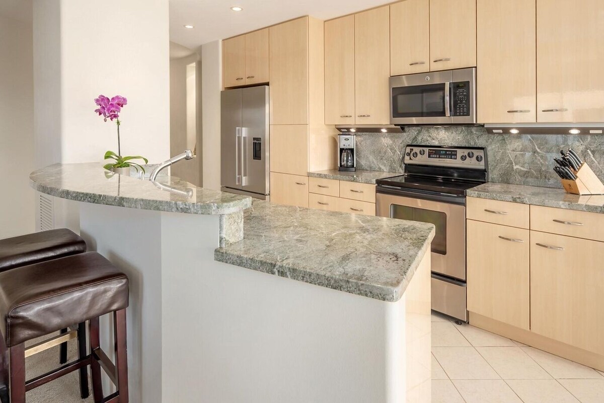 A modern kitchen with a built-in island, stainless steel appliances, and light wood cabinets.