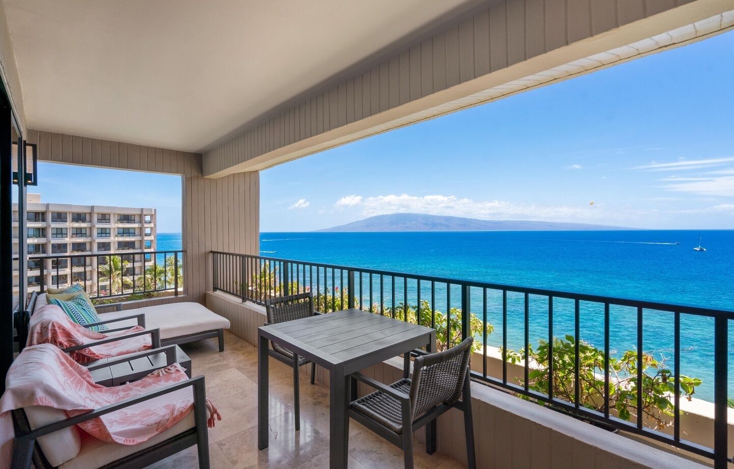 A balcony with a table and chairs, a sofa, and a view of the ocean and distant buildings.