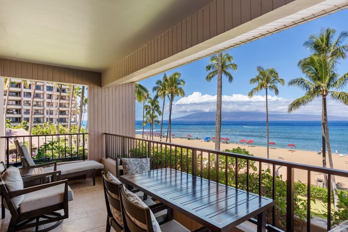 Ein Balkon mit Blick auf einen Strand, Palmen und ein Hotelgebäude im Hintergrund.