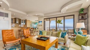 A spacious living area with a large sofa, a coffee table, and a dining area with chairs. - Kaanapali Alii-2 Bedroom Ocean Front Views (Lahaina)