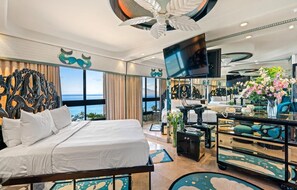 Ein Hotelzimmer mit Bett, Fernseher, Schreibtisch und Meerblick.