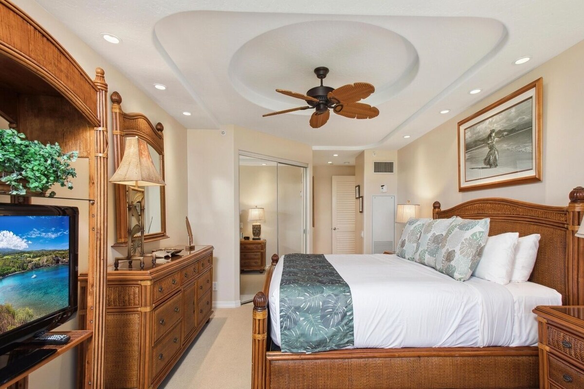 A hotel room with a bed, wooden furniture, a ceiling fan, a television, and a painting on the wall.