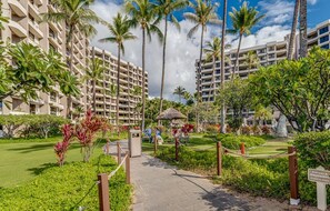 A hotel entrance with a paved pathway, palm trees, and a thatched-roof structure. - Kaanapali Alii-3 Bedroom Ocean Views (Lahaina)