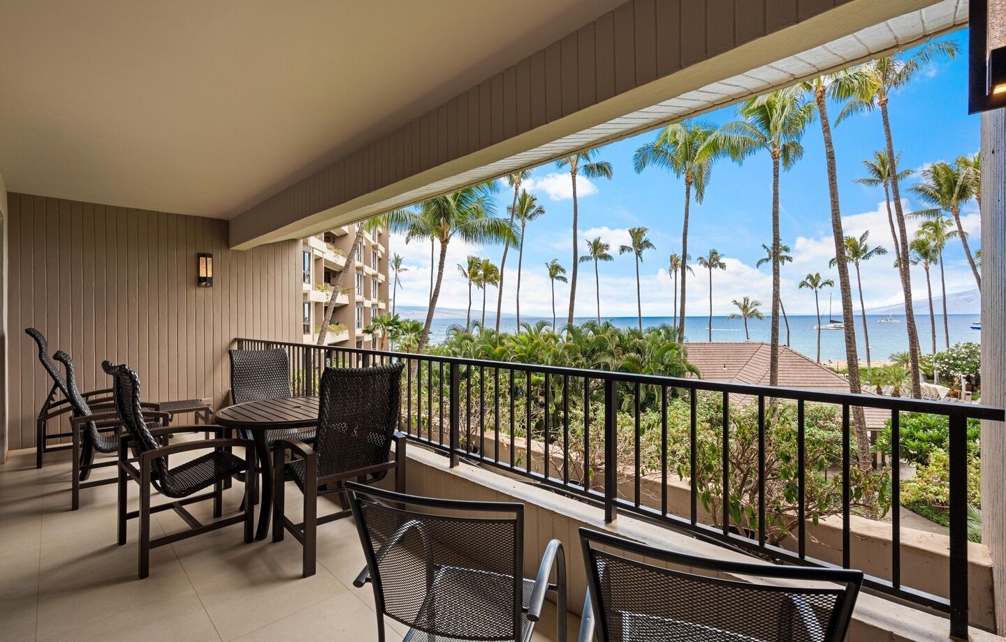 A balcony with a view of the ocean and palm trees, furnished with wicker chairs and a table.