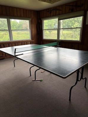 A ping pong table in a room with wooden walls and large windows.