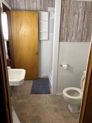 A bathroom with a wooden door, a white toilet, a white sink, and a shower area.