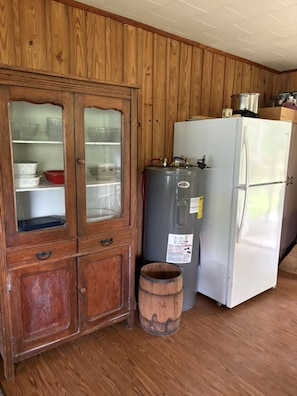 Una cocina con paneles de madera, un armario con puertas de vidrio, un calentador de agua gris, un refrigerador blanco y un barril de madera.