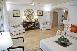 Una sala de estar con sofá, sillones, una mesa de centro, un aparador y un espejo decorativo.