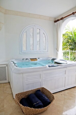 Un cuarto de spa con un jacuzzi, una cesta tejida con toallas y una ventana con vistas a la vegetación.