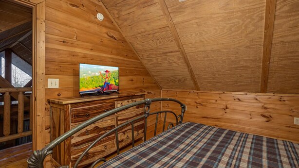 Ein Holzblockhaus-Innenraum mit einem Bett, einer Kommode und einem Fernseher, der einen Zeichentrickcharakter zeigt.
