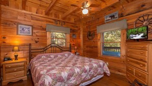 A wooden cabin bedroom with a bed, dresser, nightstands, and a ceiling fan. - Hawks Nest #1907 (Sevierville)