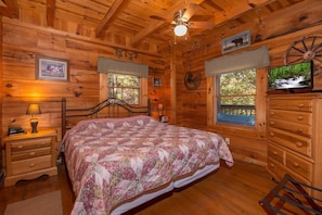 Ein Schlafzimmer einer Holzhütte mit einem Bett, einem Schminktisch, Nachttischen und einem Deckenventilator.