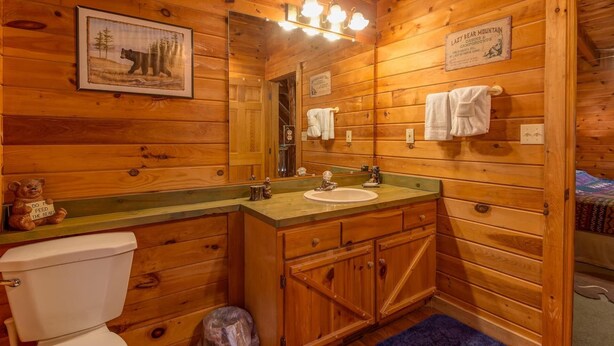 A wooden cabin bathroom with a sink, toilet, and a mirror. - Hawks Nest #1907 (Sevierville)