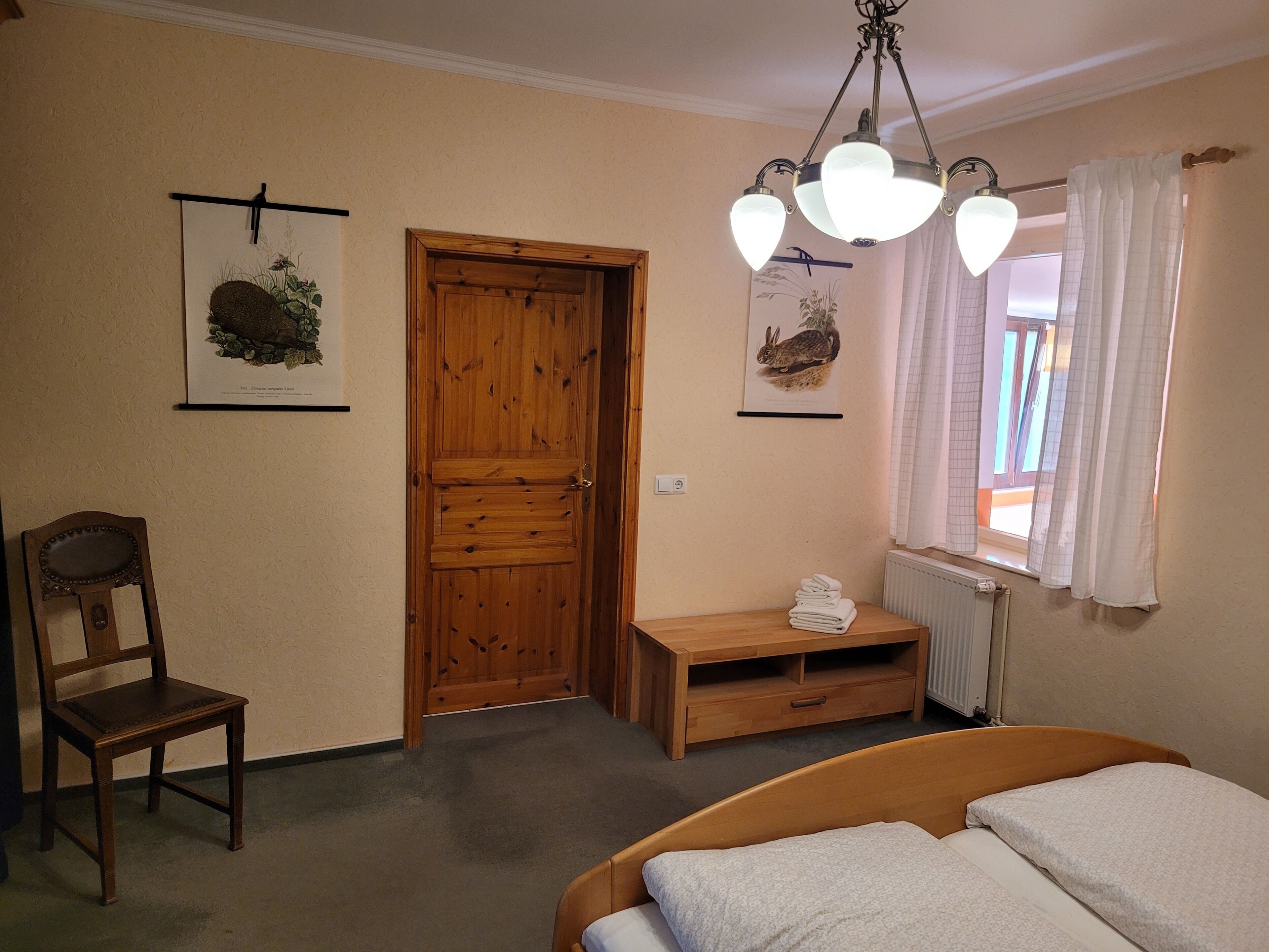 Ein Schlafzimmer mit Holztür, einem Sessel, einem Nachttisch mit Handtüchern, einem Bett und zwei Wandleuchten.