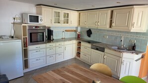 A kitchen with white cabinets, a wooden table, and a microwave. - Cozy vacation apartment in the Hoher Fläming Nature Park with a spacious garden (Wiesenburg/Mark)