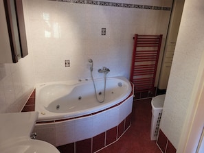 Um banheiro com banheira, vaso sanitário e um porta-toalhas vermelho.