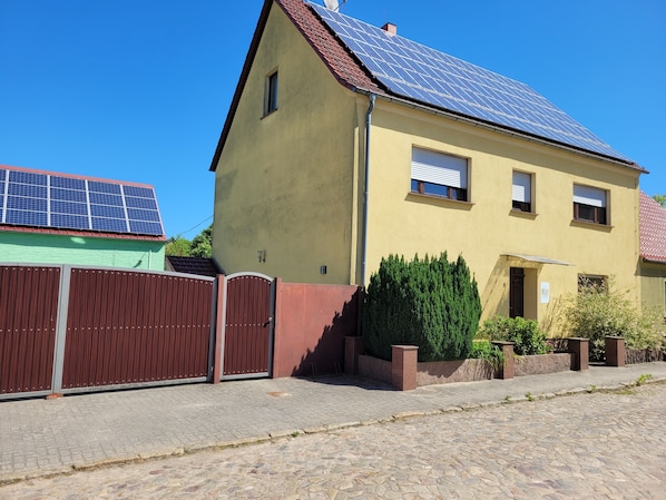 Um edifício amarelo com telhado vermelho, entrada protegida por portão e painéis solares no telhado.