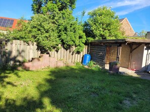 Ein Garten mit Holzzaun, blauem Fass, Gartenhaus und Baum.