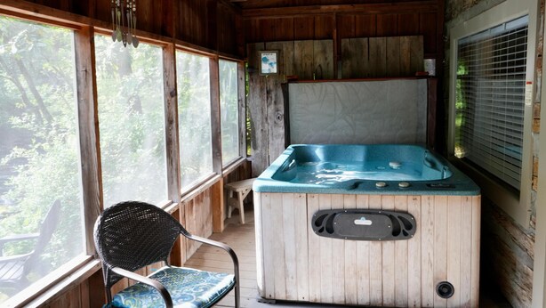 A wooden cabin with a hot tub, a chair, and large windows overlooking greenery. - Granny's River Retreat #458 (Gatlinburg)