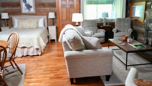 A log cabin-style room with a bed, two armchairs, a sofa, a wooden dining table, and a lamp. - Granny's River Retreat #458 (Gatlinburg)