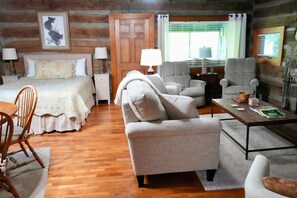 Ein rustikal eingerichtetes Zimmer im Chalet-Stil mit einem Bett, zwei Sesseln, einem Sofa, einem Holzesstisch und einer Lampe.