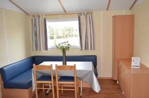 Ein Zimmer mit einem blauen Sofa, zwei Holzsesseln, einem kleinen Tisch mit einer Vase, einem Fenster mit Vorhängen und einem Schrank.