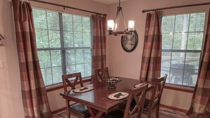 A dining room with a wooden table and chairs, plaid curtains, and a view through the windows. - Winter Haven #1903 (Gatlinburg)