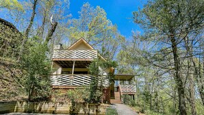 A two-story cabin with a sloped roof, surrounded by dense forest. - Winter Haven #1903 (Gatlinburg)