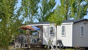 A mobile home with a small porch, a table with chairs, and a blue umbrella. - Camping 3 étoiles - Parc aquatique - ccbg0hd (Garganvillar)
