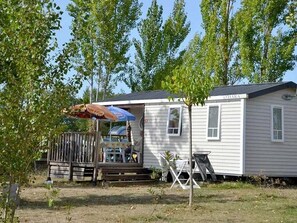Ein Mobilheim mit einer kleinen Veranda, einem Tisch mit Stühlen und einem blauen Sonnenschirm.