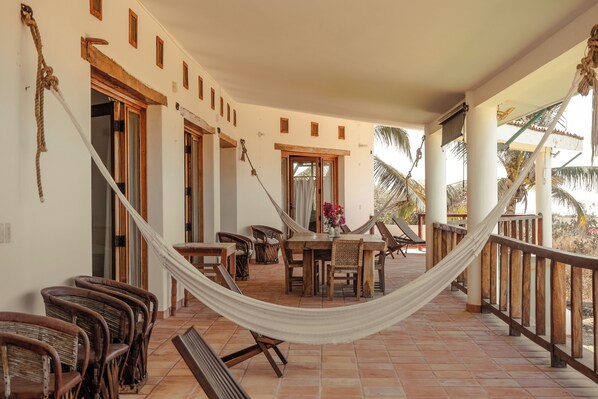 A covered outdoor area with a hammock, wooden chairs, a table with a vase, and a view of palm trees. - Beach house with pool El Cortijo (Puerto Escondido)