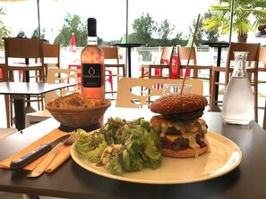 A dining table with a burger, salad, and a bottle of Vignerons wine. - Camping 3 étoiles - Parc aquatique - ccbg0hg (Garganvillar)