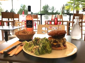A dining table with a burger, salad, and a bottle of Vignerons wine. - Camping 3 étoiles - Parc aquatique - ccbg0hh (Garganvillar)