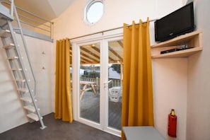 Een kamer met een schuifdeur van glas, een aan een plank bevestigde televisie, een brandblusser en een ladder tegen de muur.