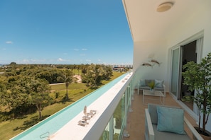A balcony with a pool, outdoor seating, and a view of a landscape with trees and buildings. - Exquisite apt : Private beach : Swimming pool : 2BR (Punta Cana)