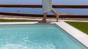 Une personne se promène au bord d’une piscine, avec vue sur la mer.