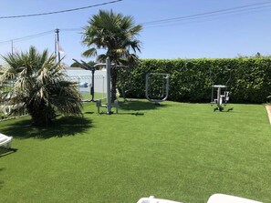 Ein gepflegter Rasen mit Fitnessgeräten, Palmen und einer Hecke.