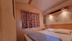 Hotellihuone, jossa on sänky, sängynpääty, seinälle kiinnitetty peili ja kuviollinen verho.