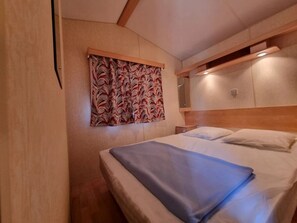 A hotel room with a bed, a headboard, a wall-mounted mirror, and a patterned curtain. - Camping 3 étoiles - ccbgcgg (Gondrin)