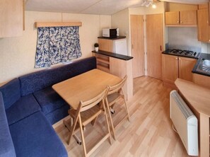 A compact kitchen with a dining area, including a table, chairs, a microwave, and a stove. - Camping 3 étoiles - ccbgcgg (Gondrin)